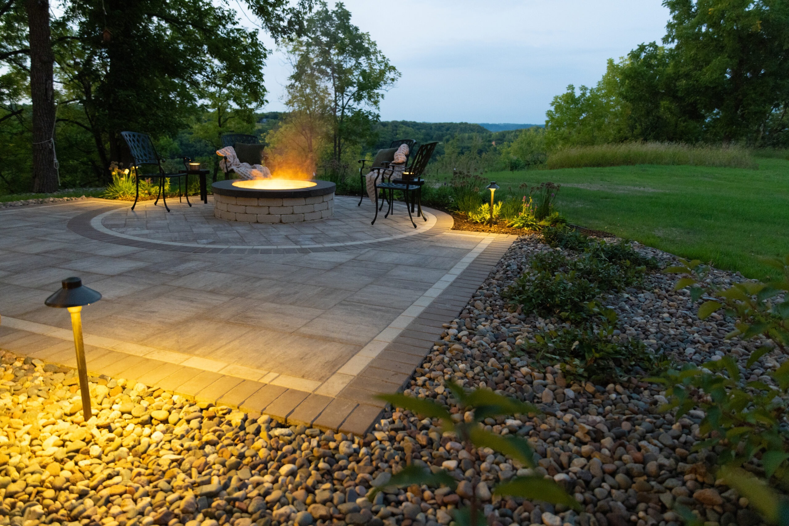 Cozy patio illuminated with landscape lighting, highlighting garden beds filled with vibrant flowers and shrubs.