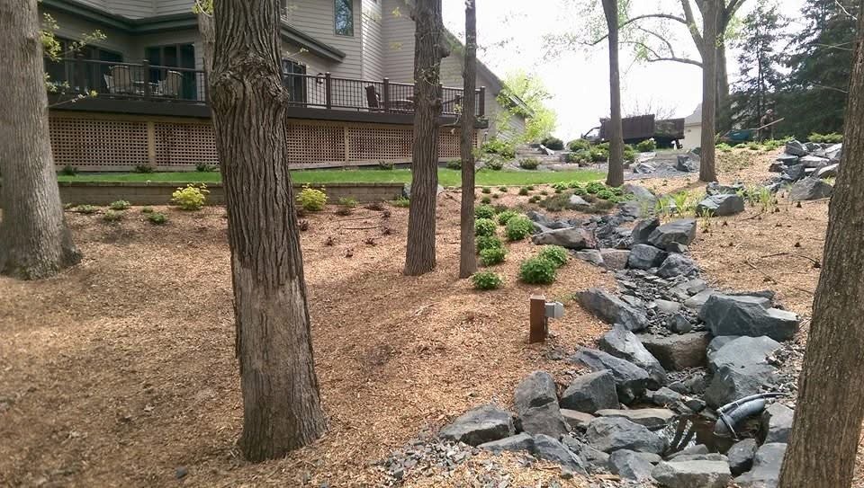 Stone-lined dry creek bed directing water through a sloped yard Landscape Drainage Solutions